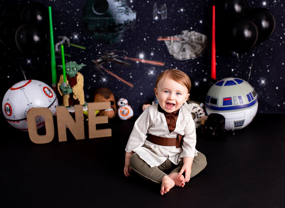 Star Wars themed first birthday photo setup with lightsabers, BB-8, and space background.