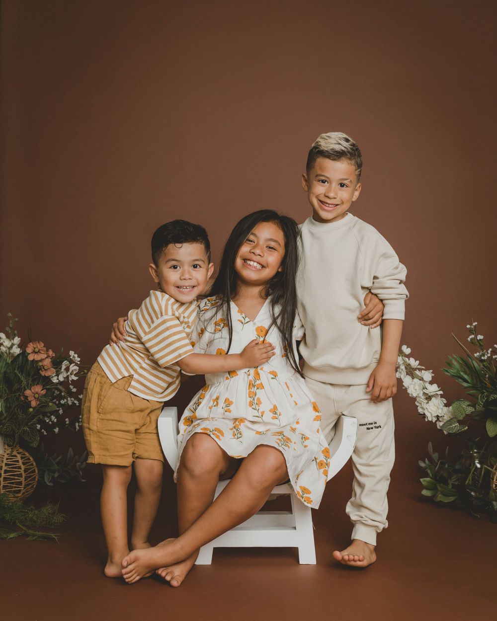 Three happy children posing together in a professional studio portrait with floral decor.
