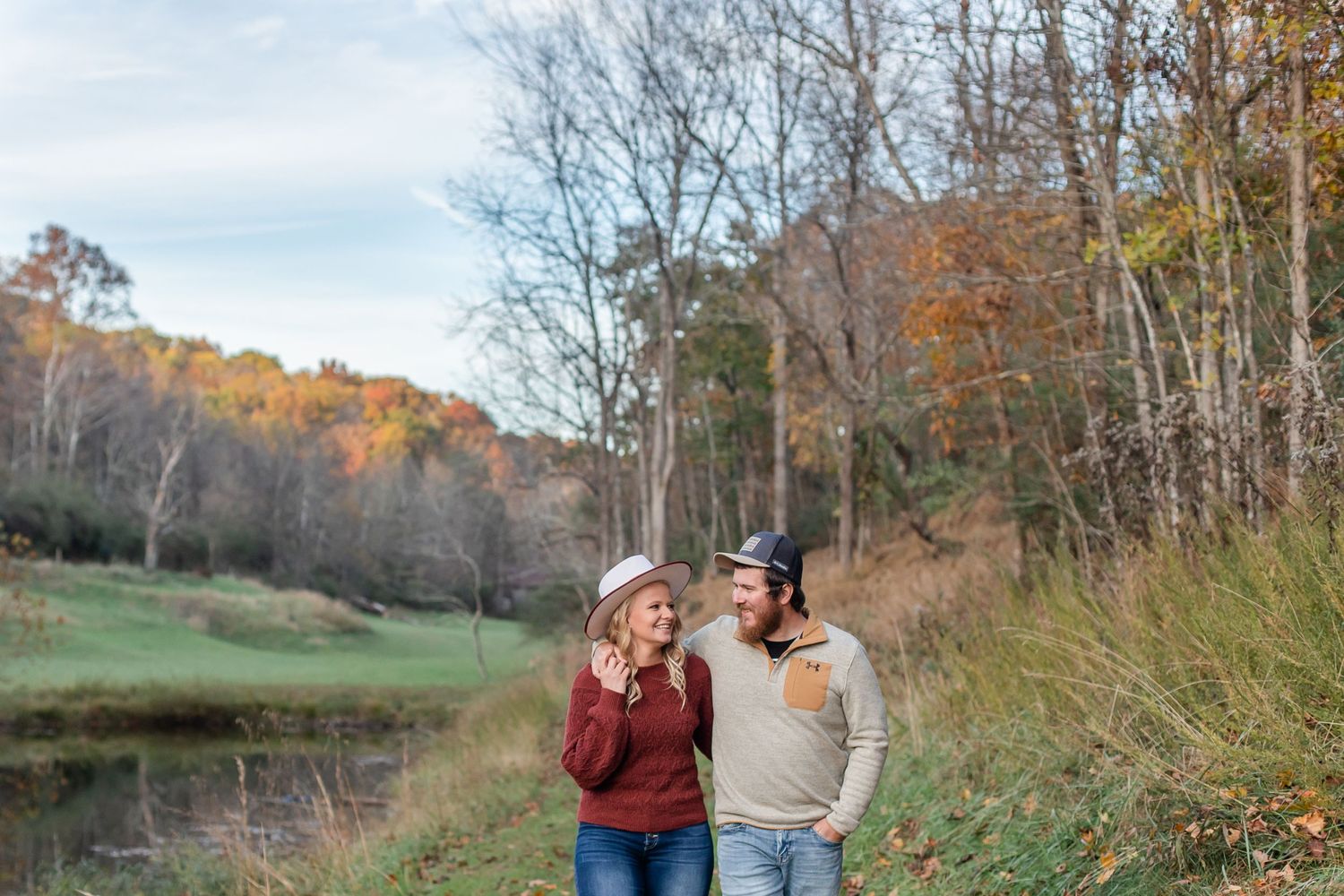 A couple shares tender moments against a backdrop of fall foliage and bare trees in a natural setting.