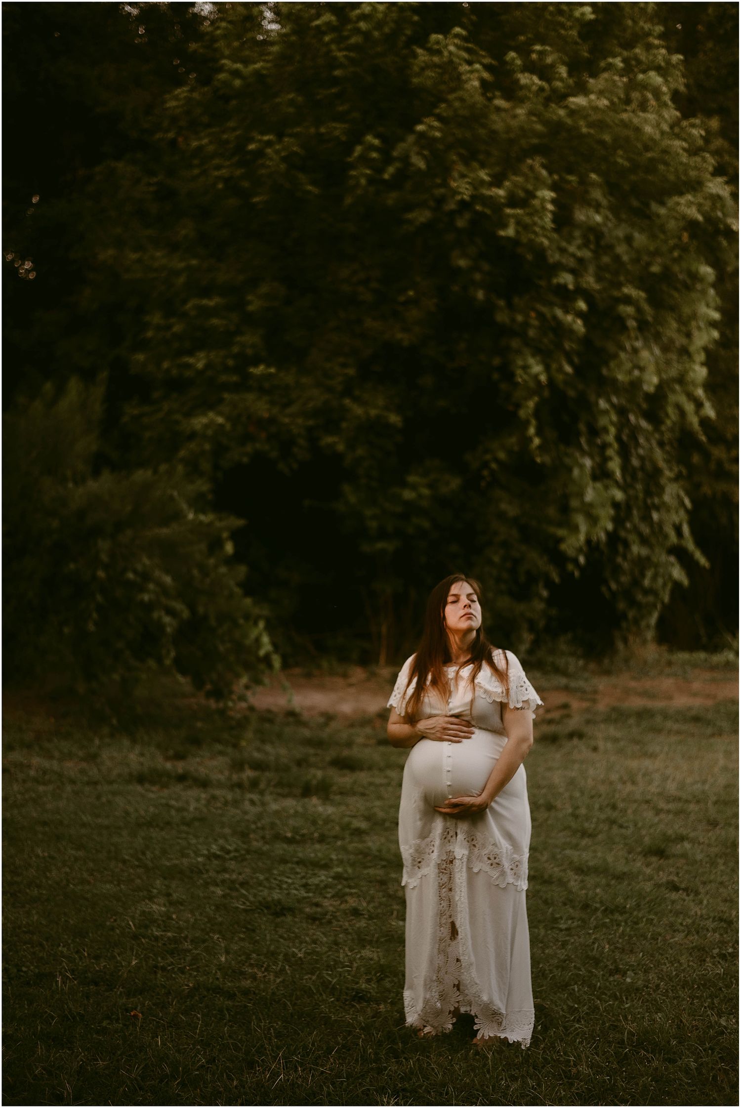 Dreamy maternity photograph featuring a floor-length white lace dress in a golden-hour garden setting.