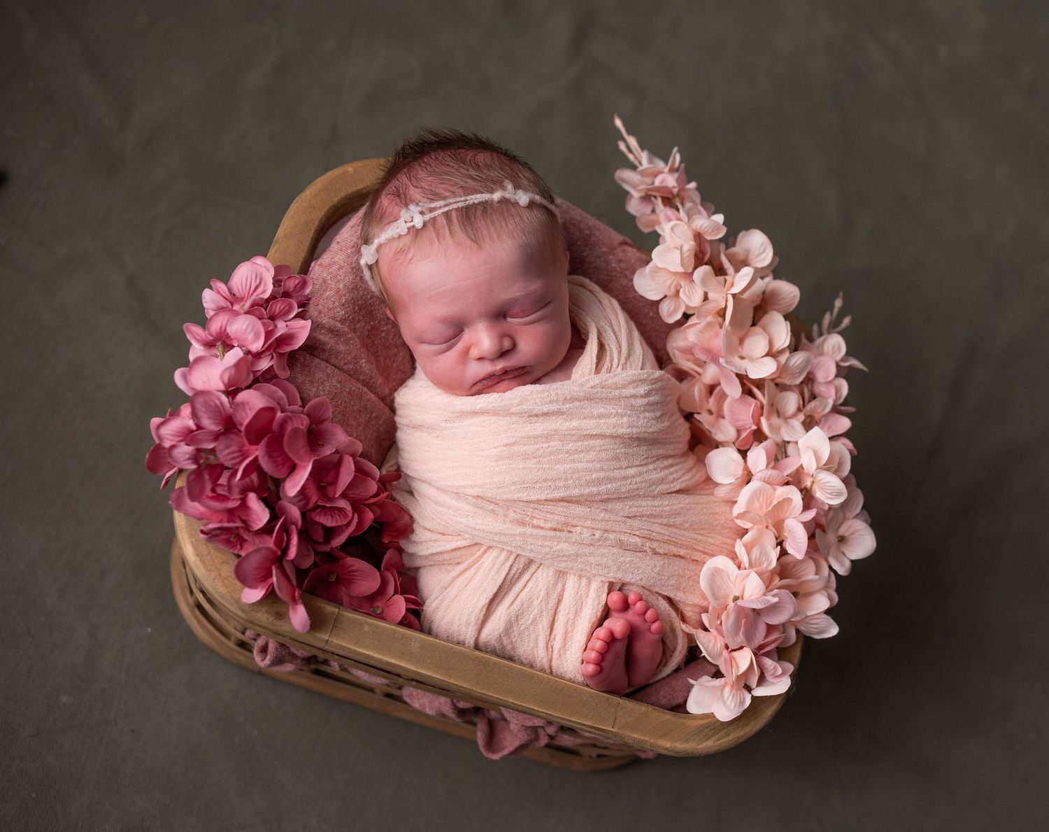Sleeping newborn wrapped in blush pink surrounded by pink flowers.
