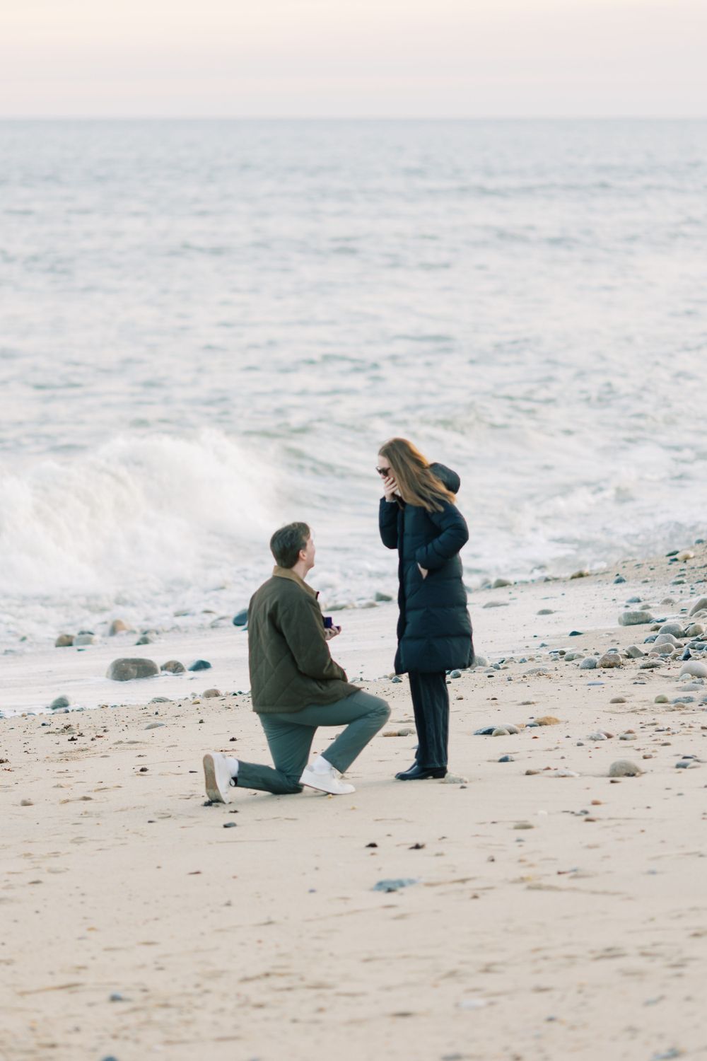 A surprise proposal moment captured on a beach with crashing waves in the background in Montauk, Long Island, New York.