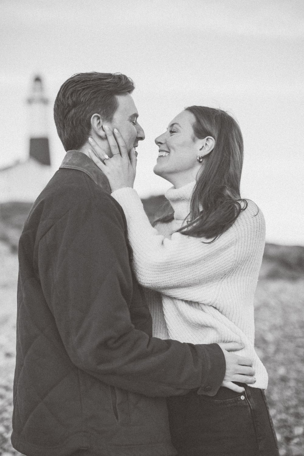 A tender moment between a couple with a lighthouse visible in the background in Montauk, Long Island, New York.