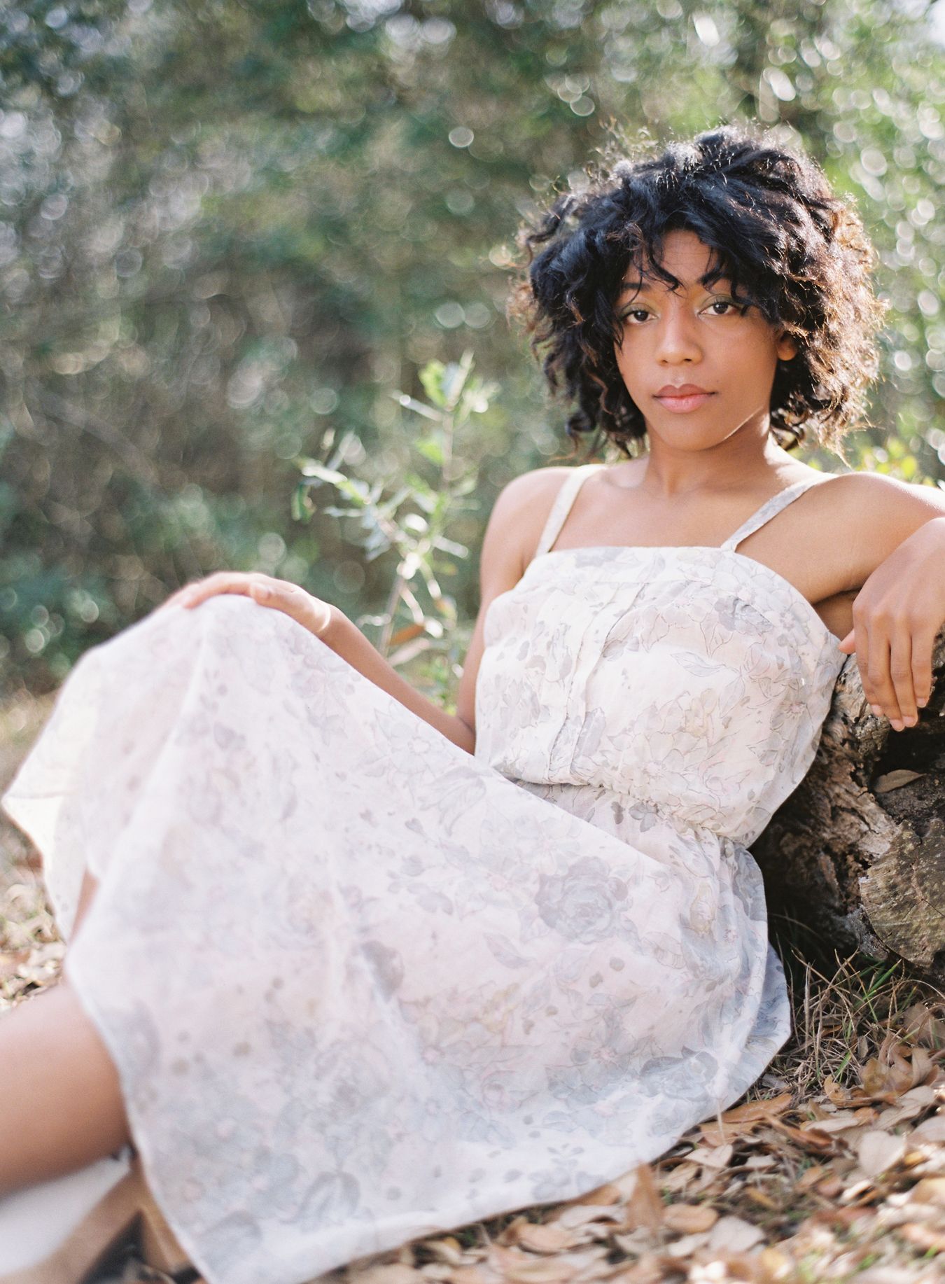 A portrait of someone in a white lace dress posing outdoors in natural lighting.