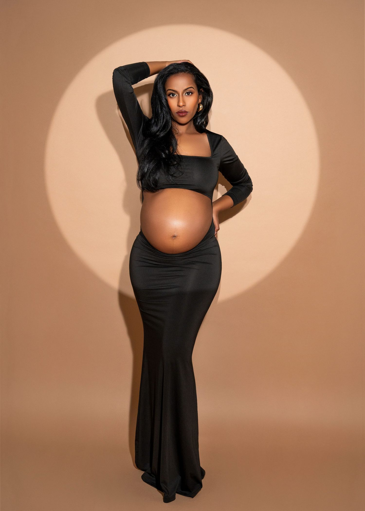 studio maternity photo shoot in minnesota a woman stands glamorously in a spotlight with a hand in her hair