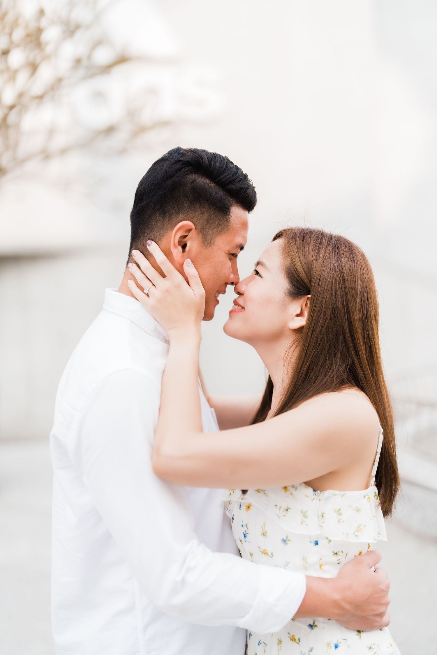 A romantic close-up moment between a couple in white outfits against a light background.
