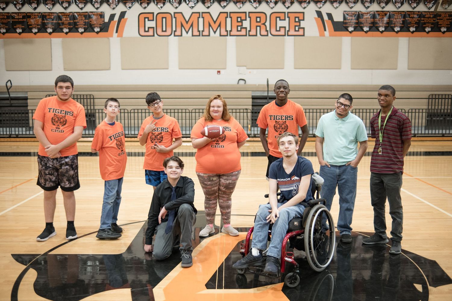 Group posed together in orange school spirit wear in gymnasium setting.