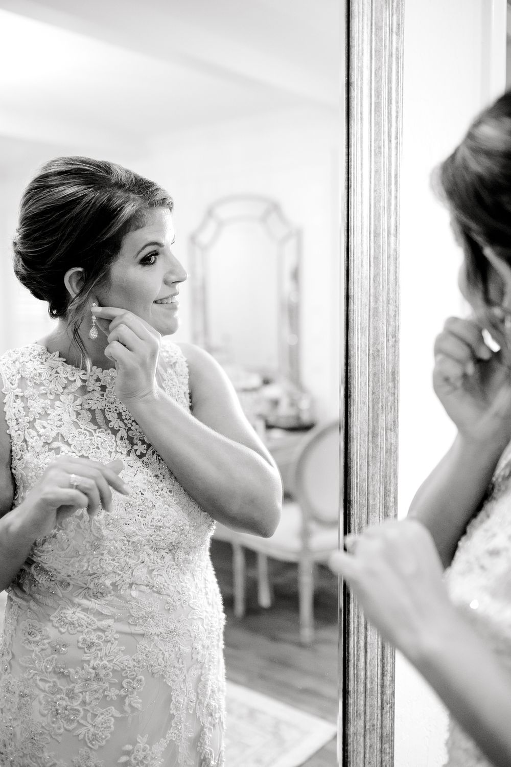 Black and white portrait of bride putting on earrings while looking in mirror.