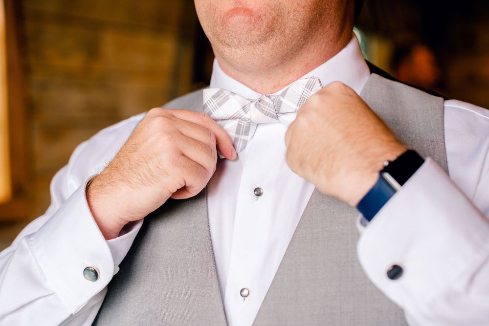 Close-up detail shot of hands adjusting a white bow tie on a formal gray suit.