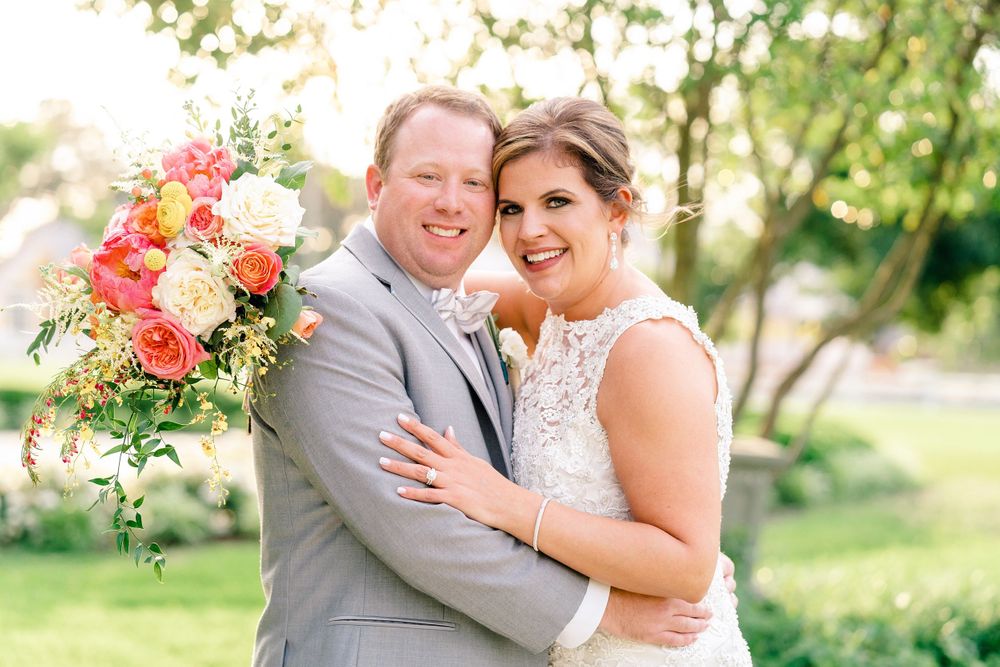A joyful wedding portrait outdoors featuring a colorful coral bouquet and elegant attire.