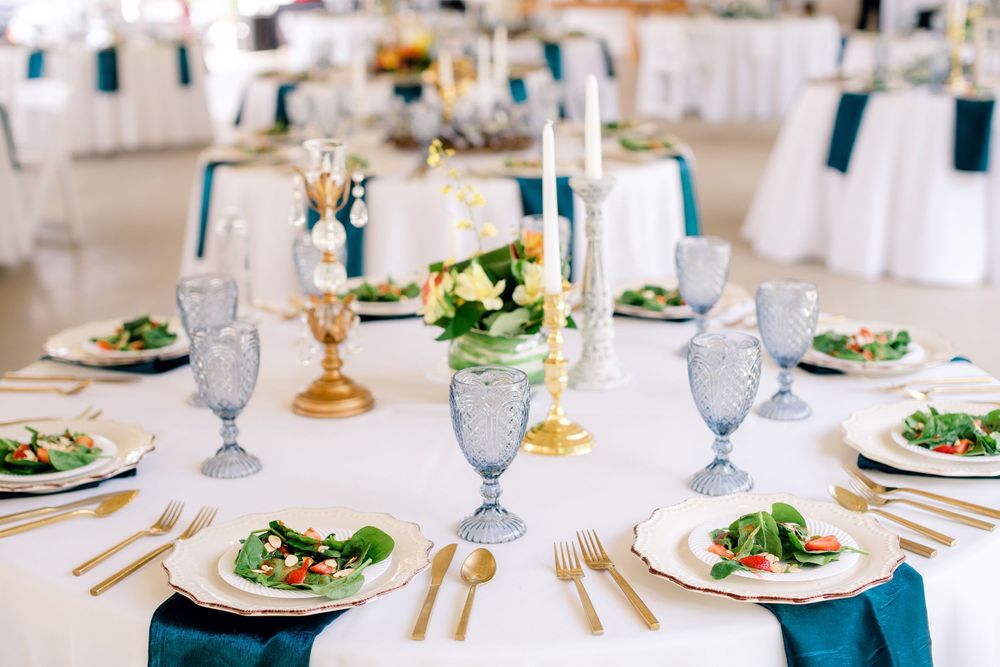 An elegant wedding table setting with blue accents, crystal glasses and gold flatware.