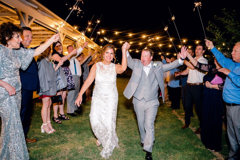 Newlyweds exit through sparkler tunnel at night under string lights.