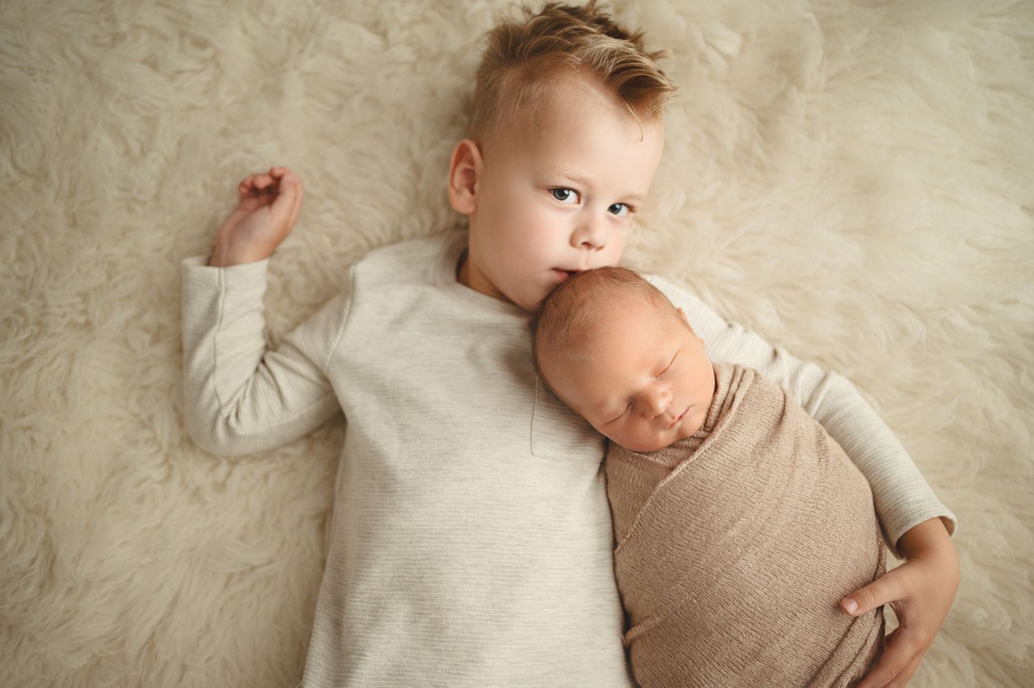 Two young siblings posing together on a textured beige background in matching light outfits.