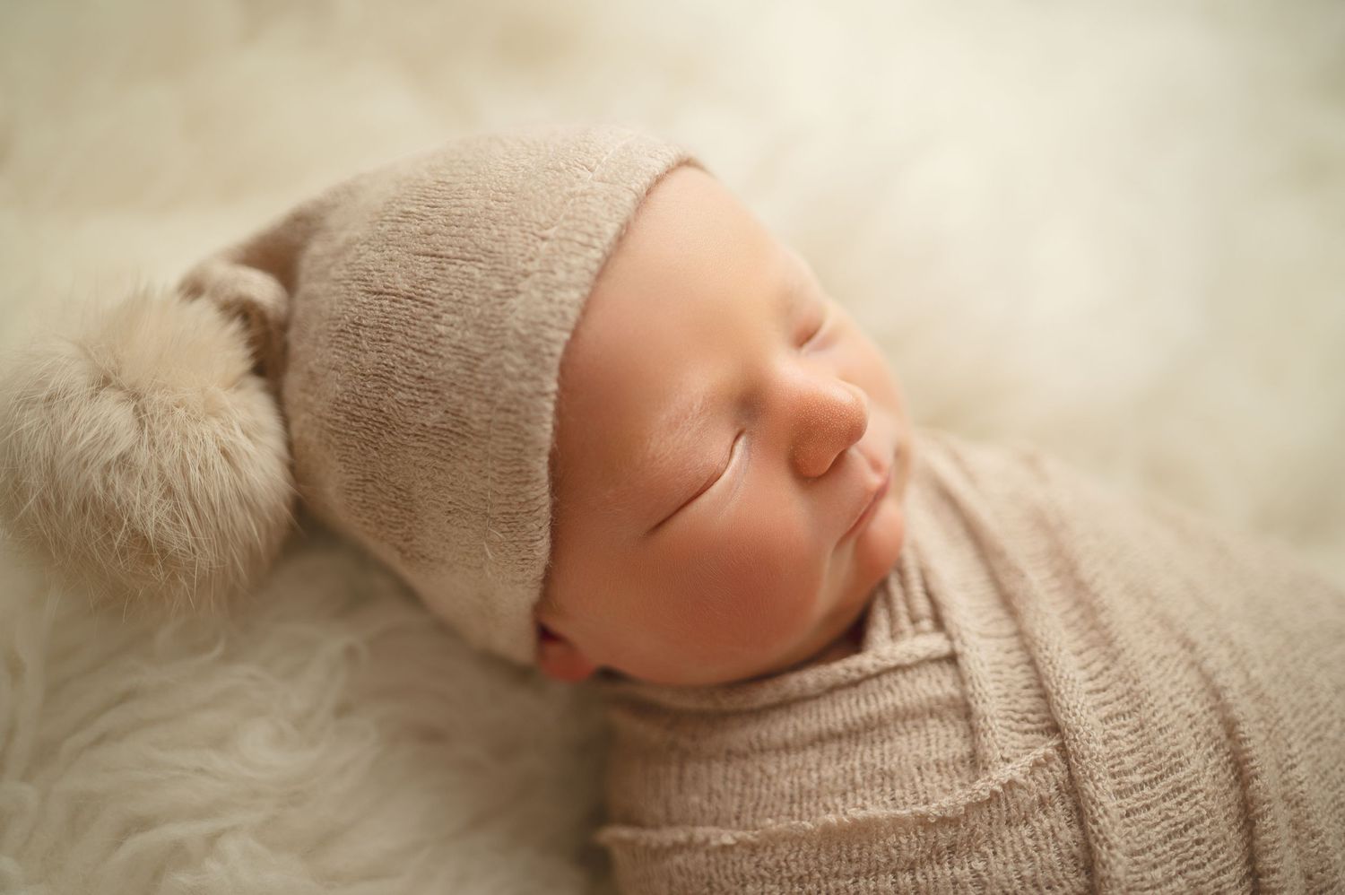 Sleeping newborn wearing a beige hat on soft furry backdrop.