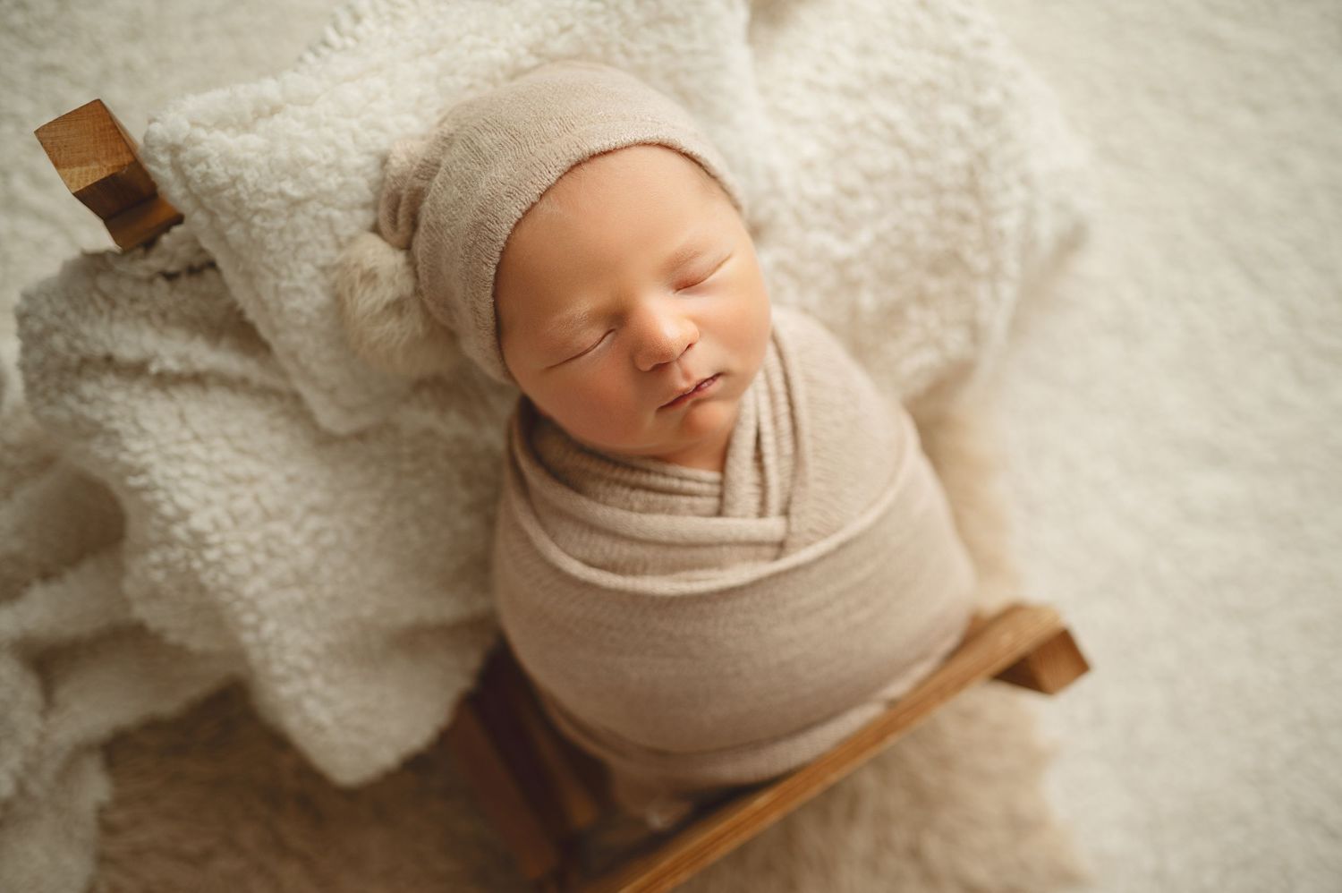 Peaceful newborn wrapped in beige fabric sleeping on white textured blanket.