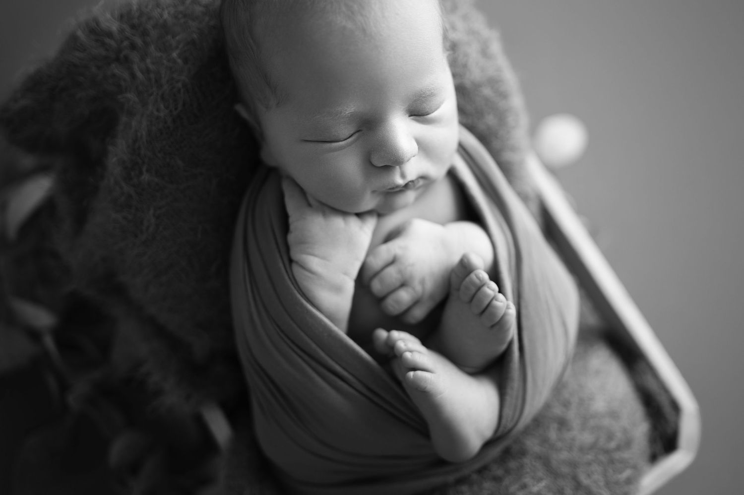 Sleeping newborn wrapped in soft fabric in black and white portrait.