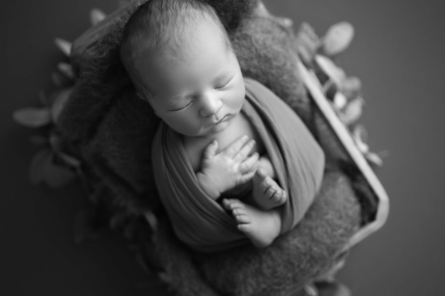 Peaceful newborn baby wrapped in fabric on textured background in black and white.