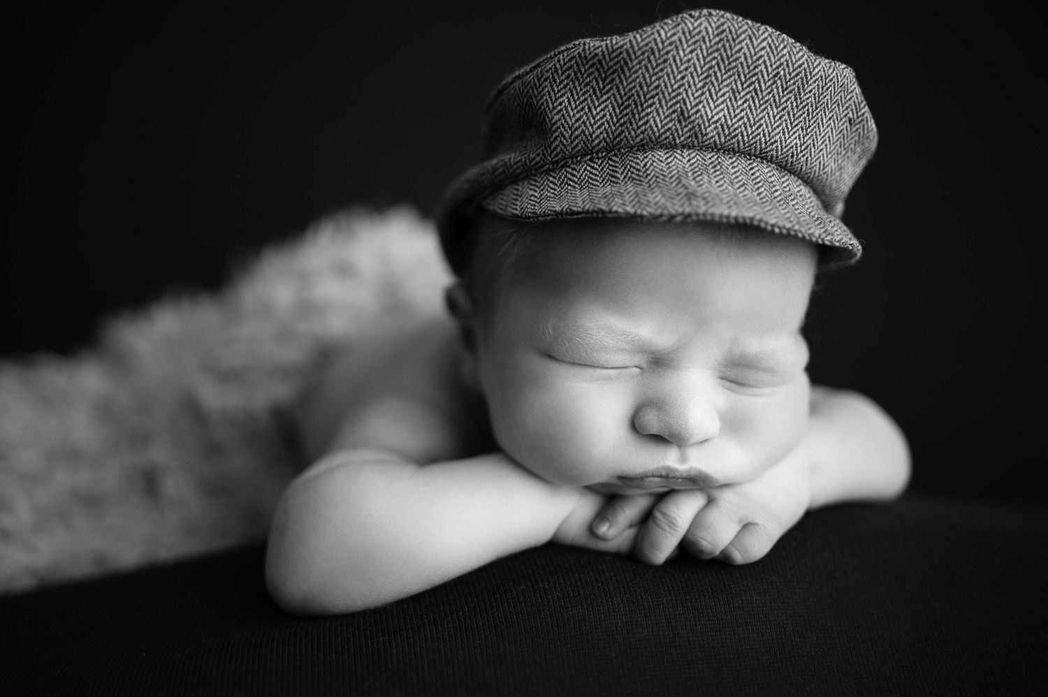 Sleeping baby wearing newsboy cap in black and white portrait.
