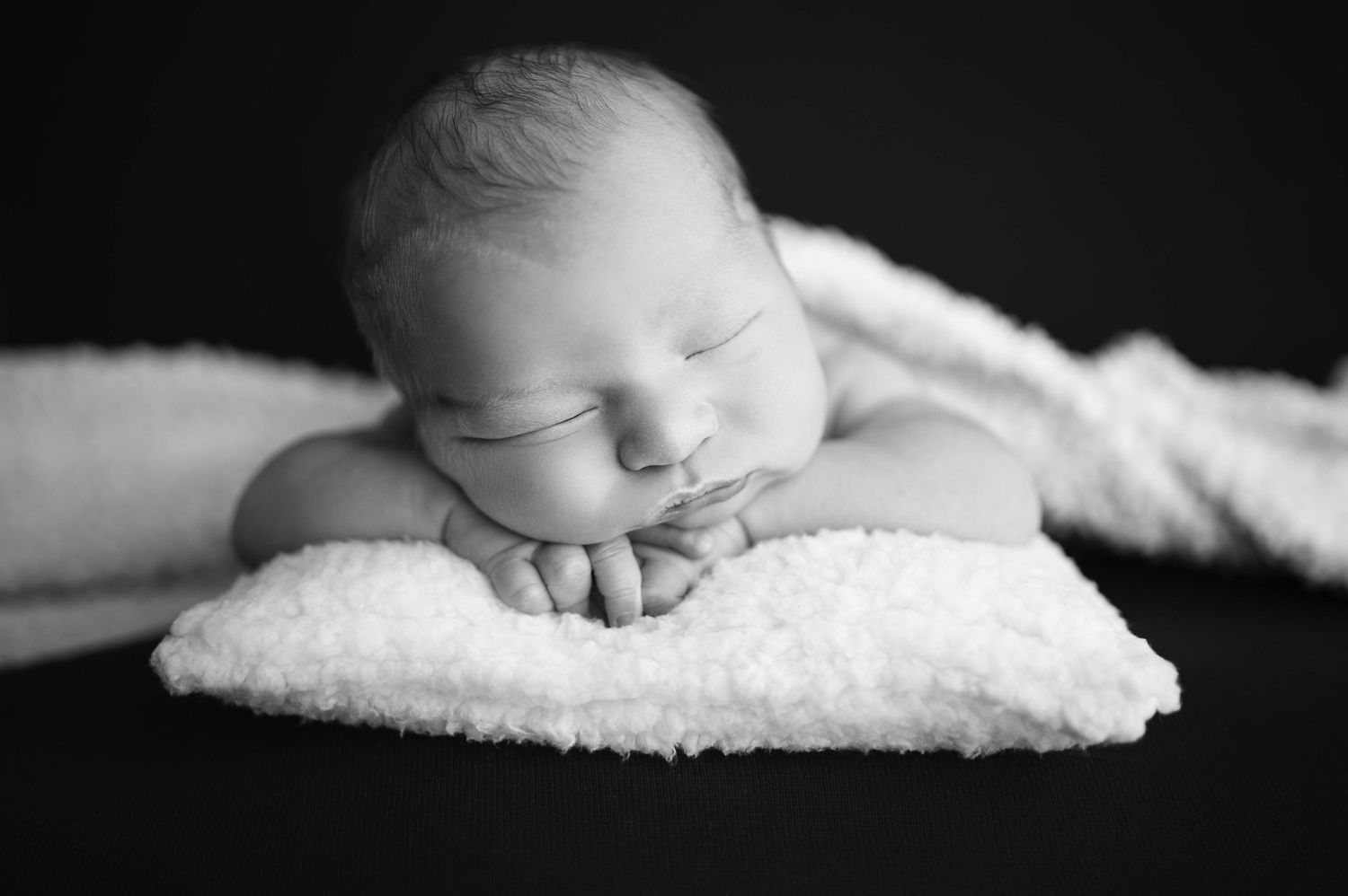 Peaceful sleeping newborn rests on soft white blanket in black and white portrait photography.