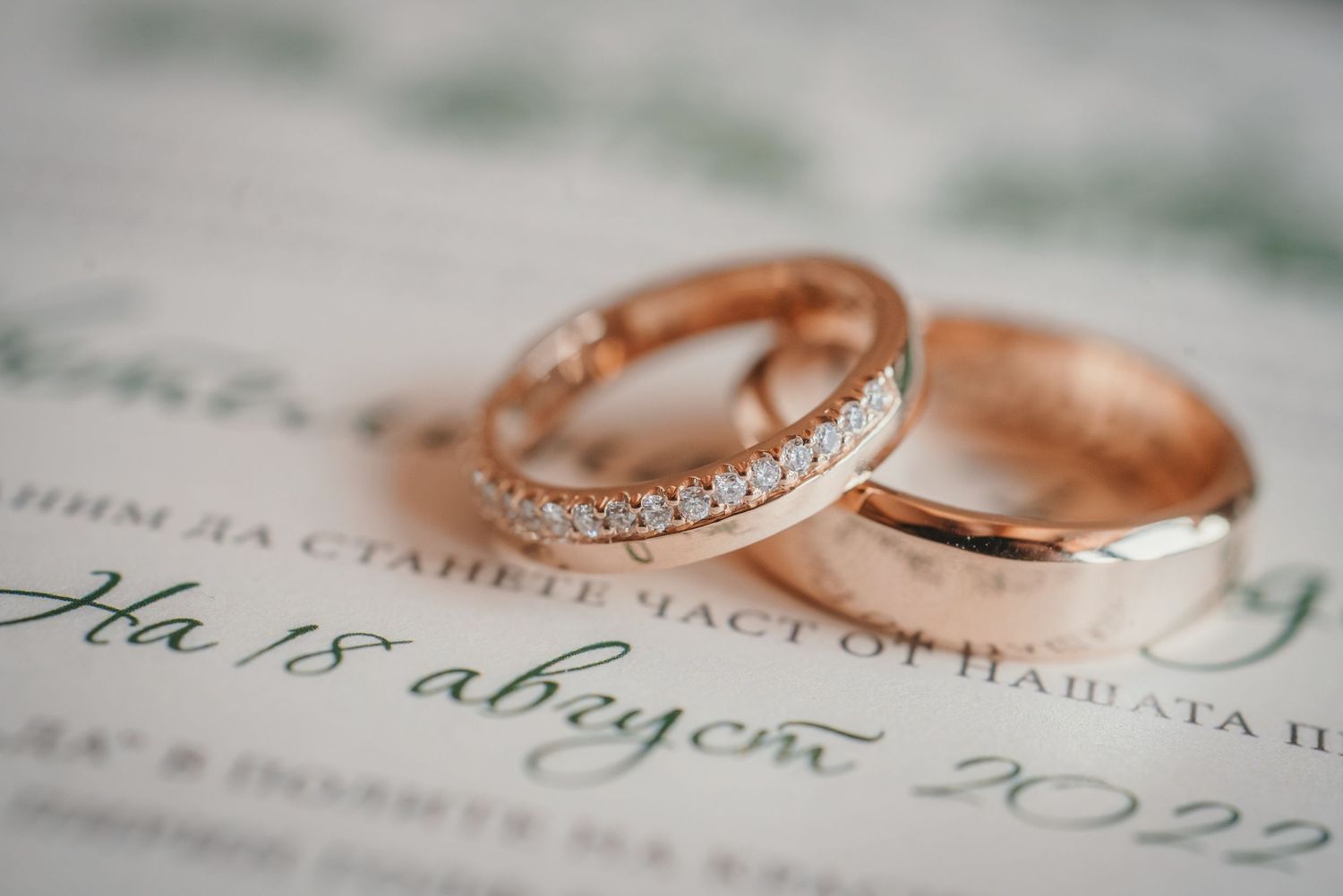 Rose gold wedding rings with diamonds displayed on printed invitation text.