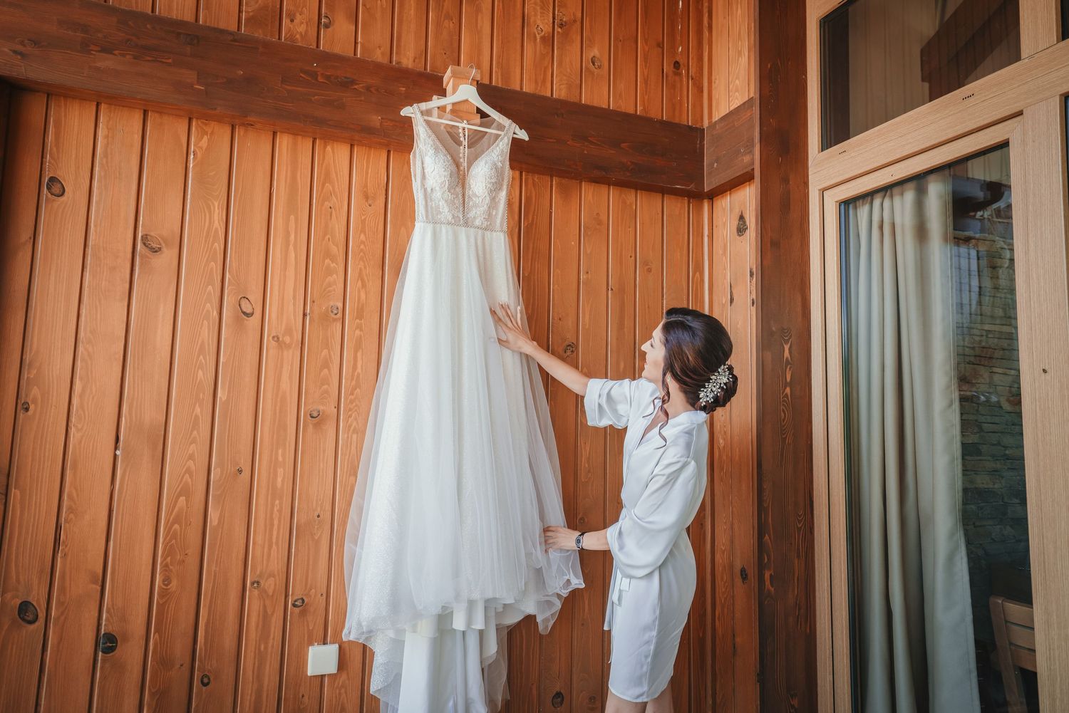 White wedding gown hanging on wooden wall while someone reaches to touch it.