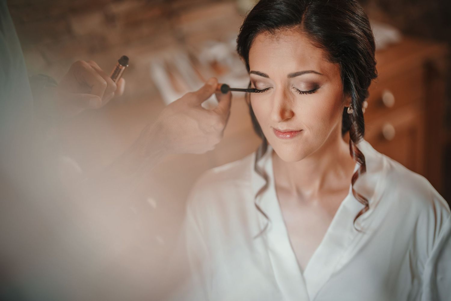 Professional makeup application in progress with soft natural lighting.