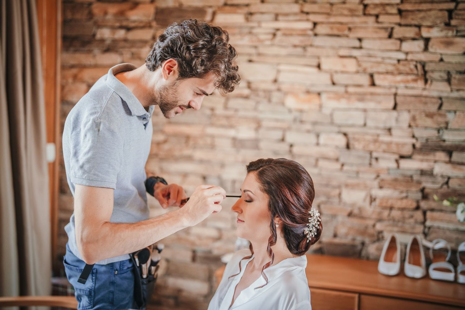 Wedding day makeup preparation scene against stone wall background.