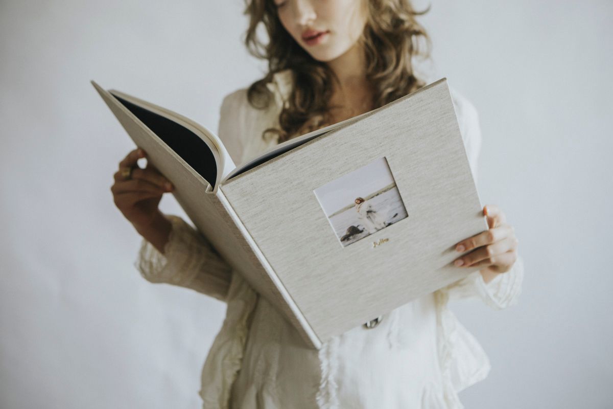 Person holding open a white wedding photo album while wearing casual attire.