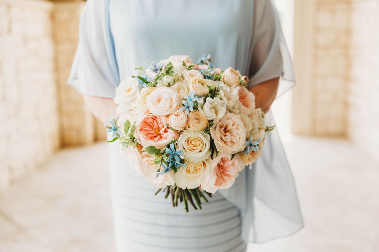 Delicate peach and white floral bouquet held against light blue fabric in an elegant setting.