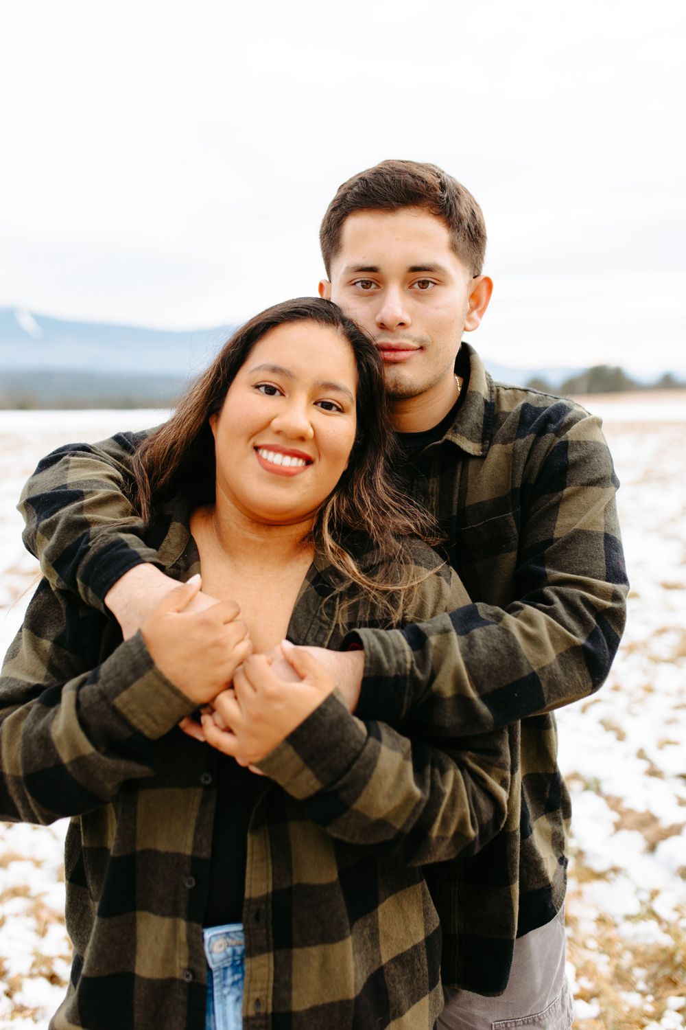 Couple in casual attire sharing an intimate moment with snowy mountains in the background.