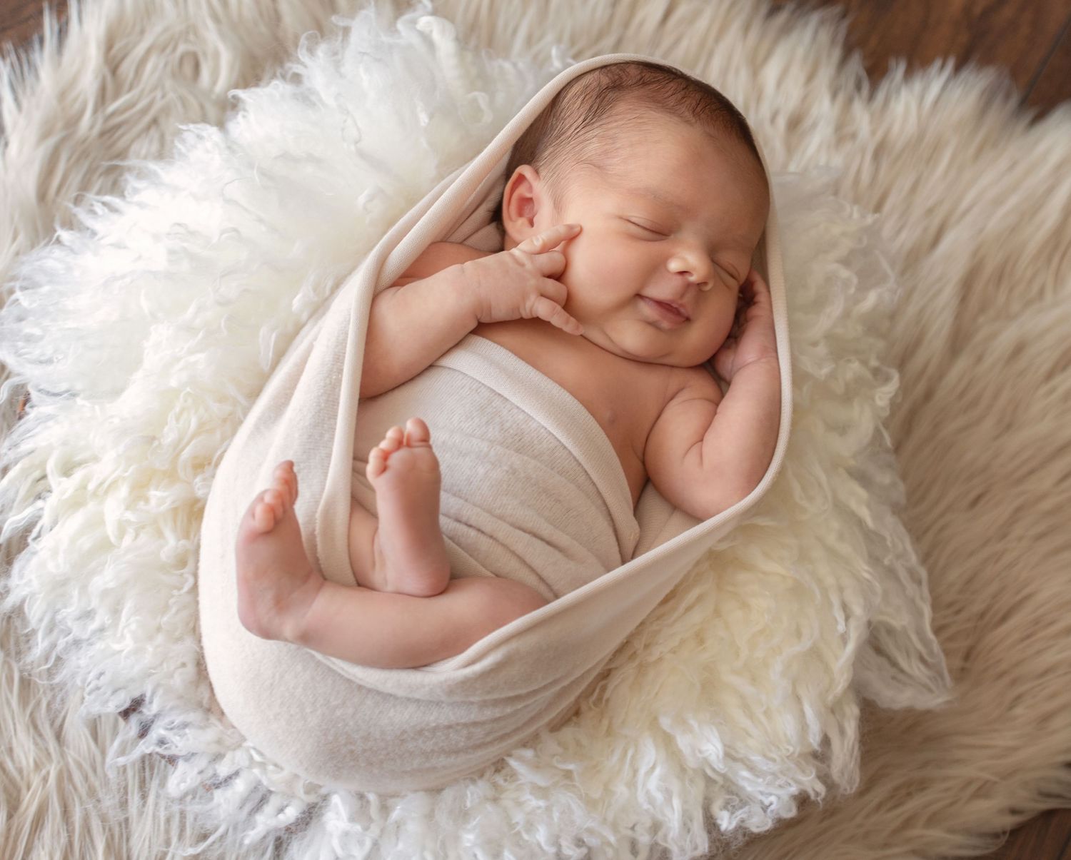 Newborn wrapped in white fabric sleeping peacefully on soft furry backdrop.