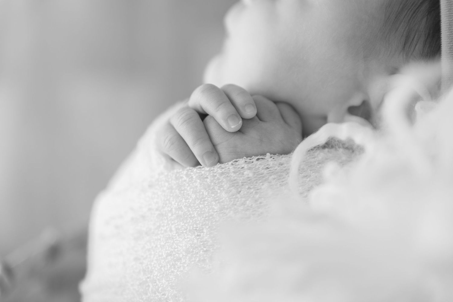 Close-up black and white image of tiny fingers grasping delicate lace fabric.