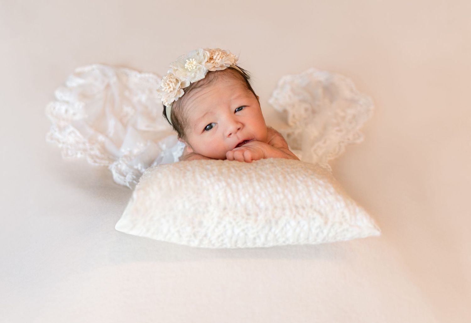 Baby wearing floral headband rests peacefully on white quilted pillow.
