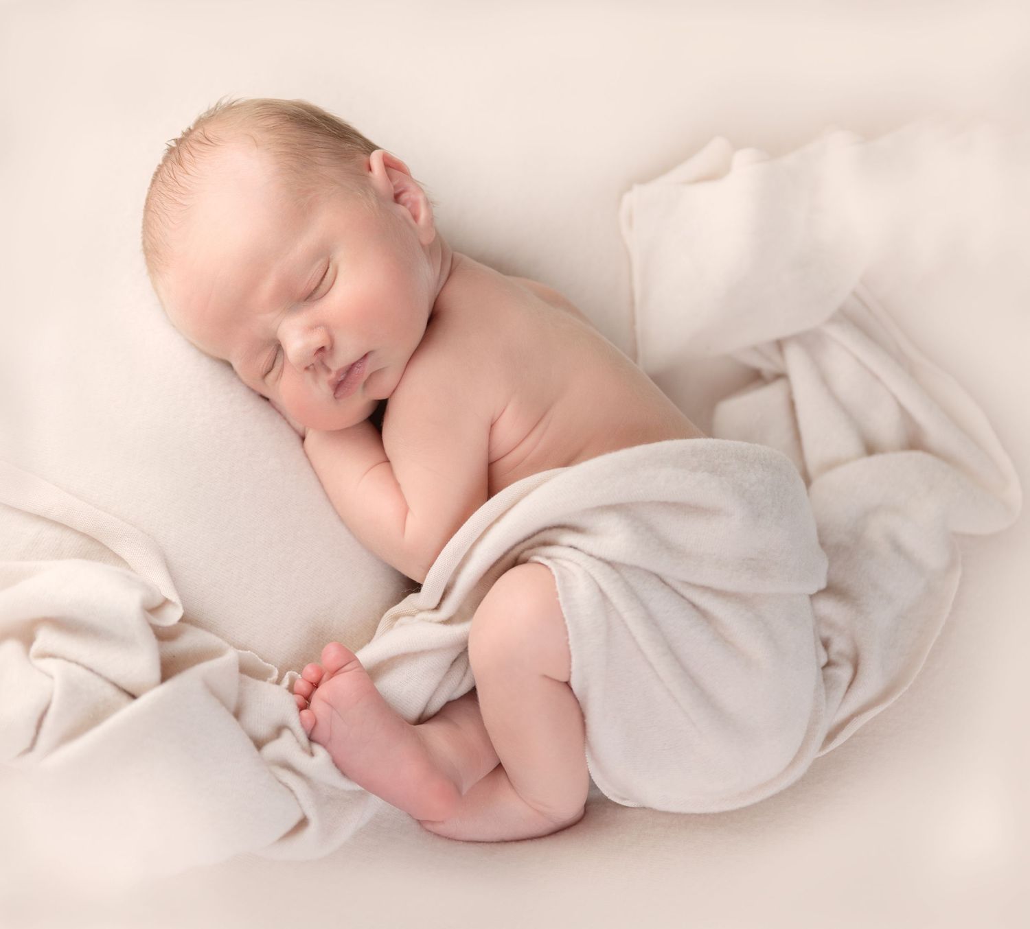 Sleeping newborn on white bedding wrapped in light fabric.