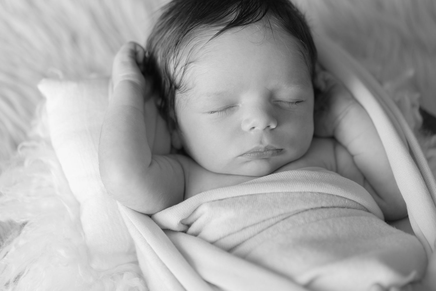 Black and white portrait of sleeping newborn wrapped in soft white fabric.