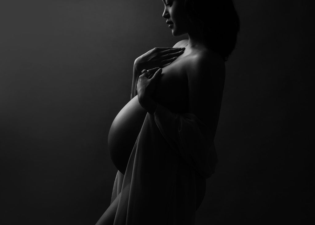 Artistic black and white silhouette of pregnant woman's belly in dramatic lighting.