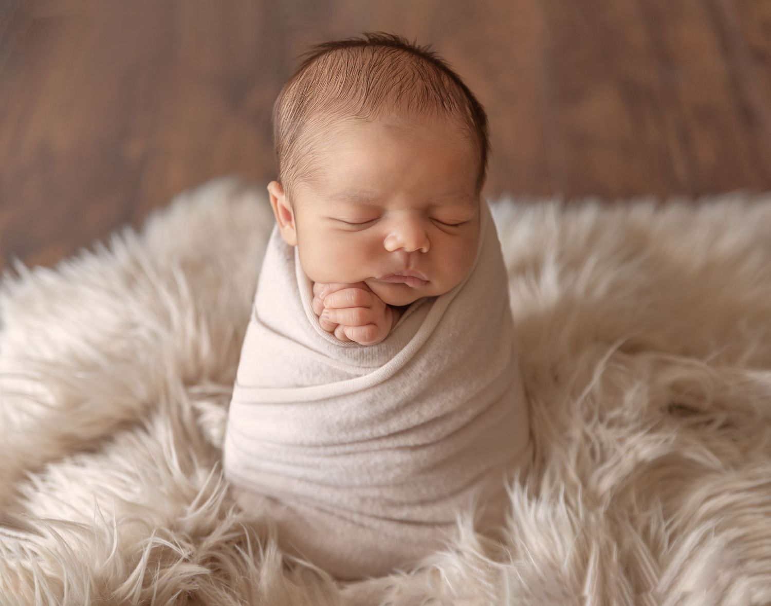 Sleeping newborn baby wrapped in soft white fabric on a furry backdrop.