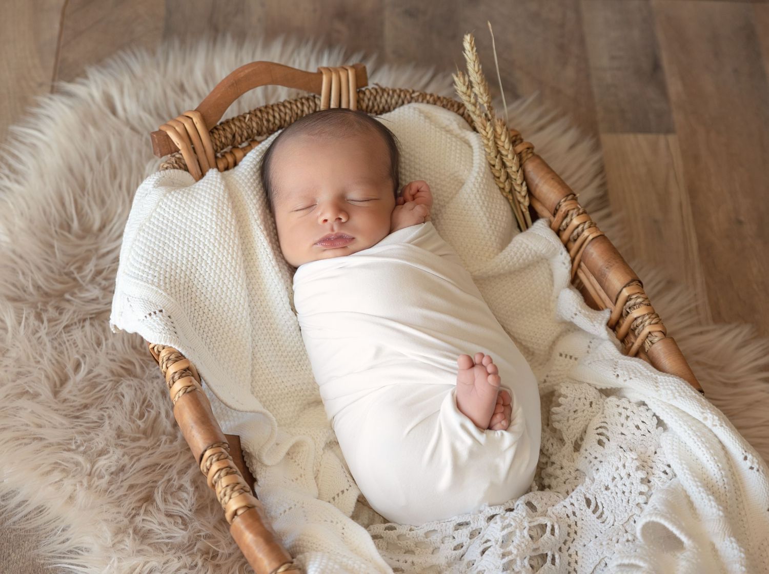 Sleeping newborn swaddled in white lying in vintage wicker basket with lace trim.