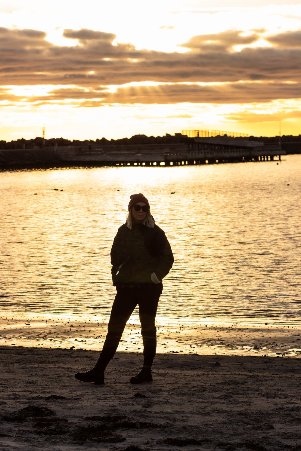 Silhouette of person standing on beach during golden hour sunset.