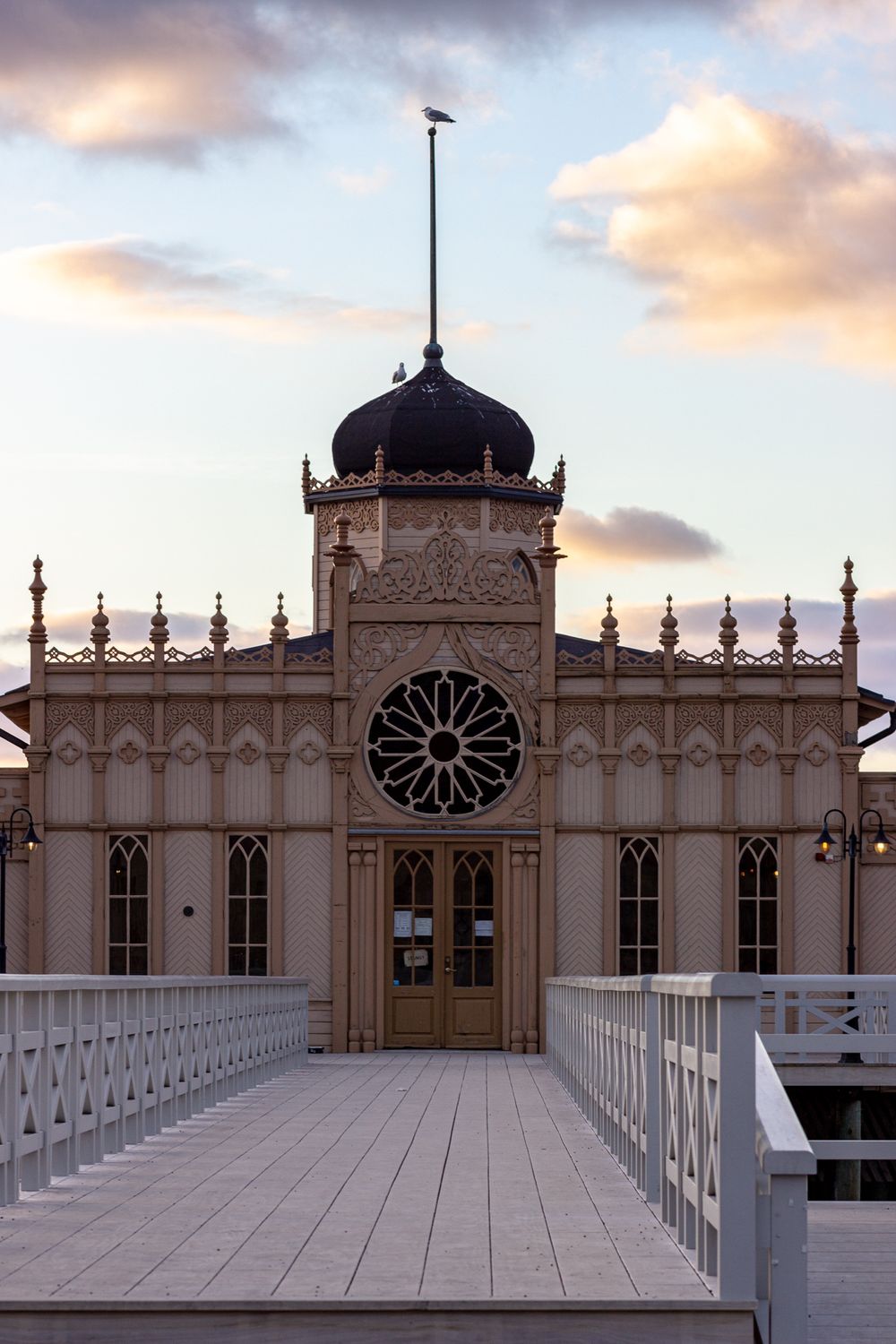Ornate Victorian-style pavilion with domed roof and white walkway at sunset.