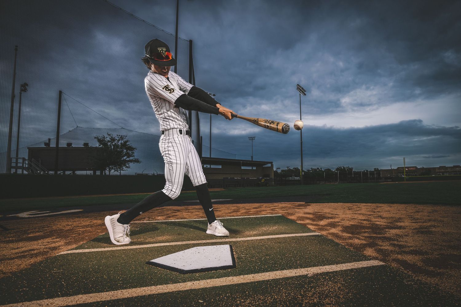 Baseball player swinging bat at home plate against stormy sky.