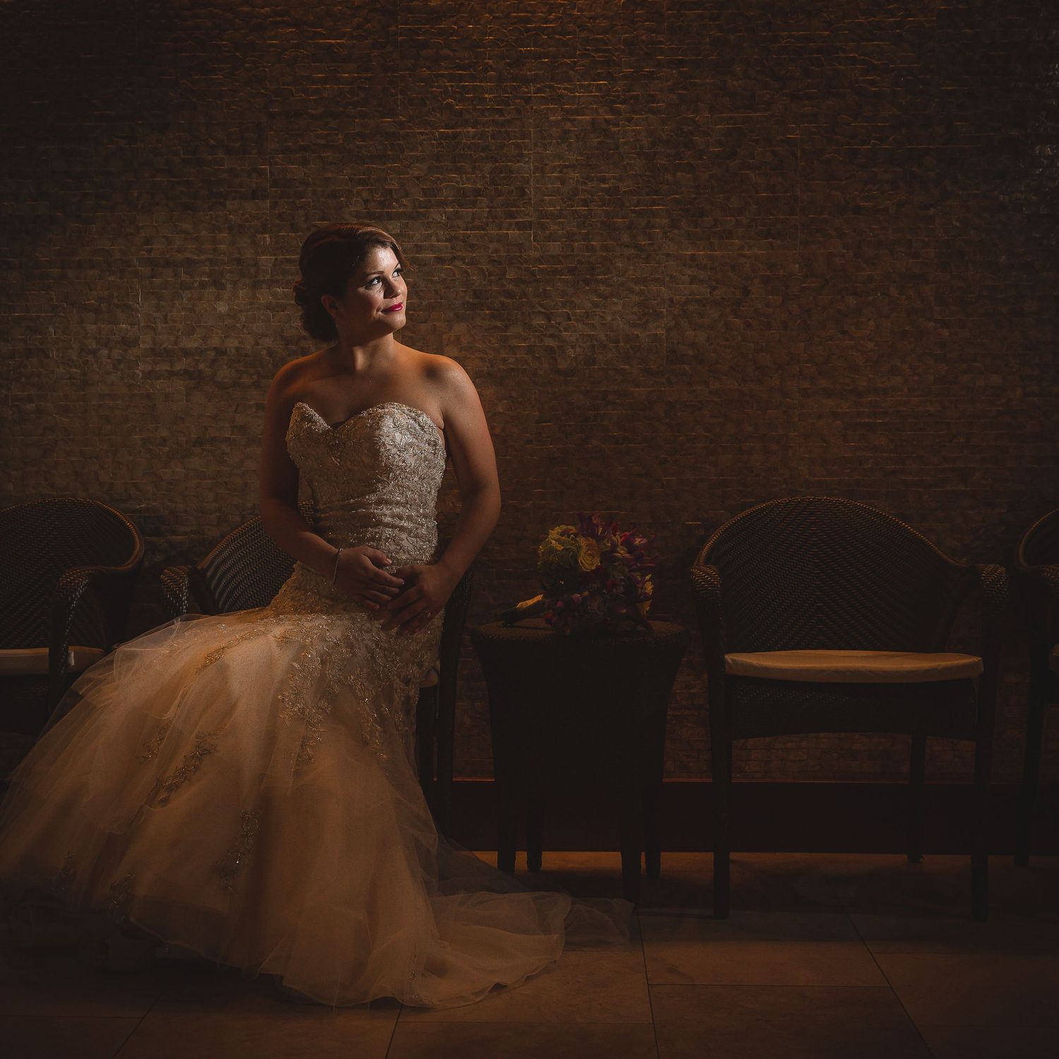 A wedding dress with a flowing tulle skirt is illuminated against a dark brick wall backdrop.