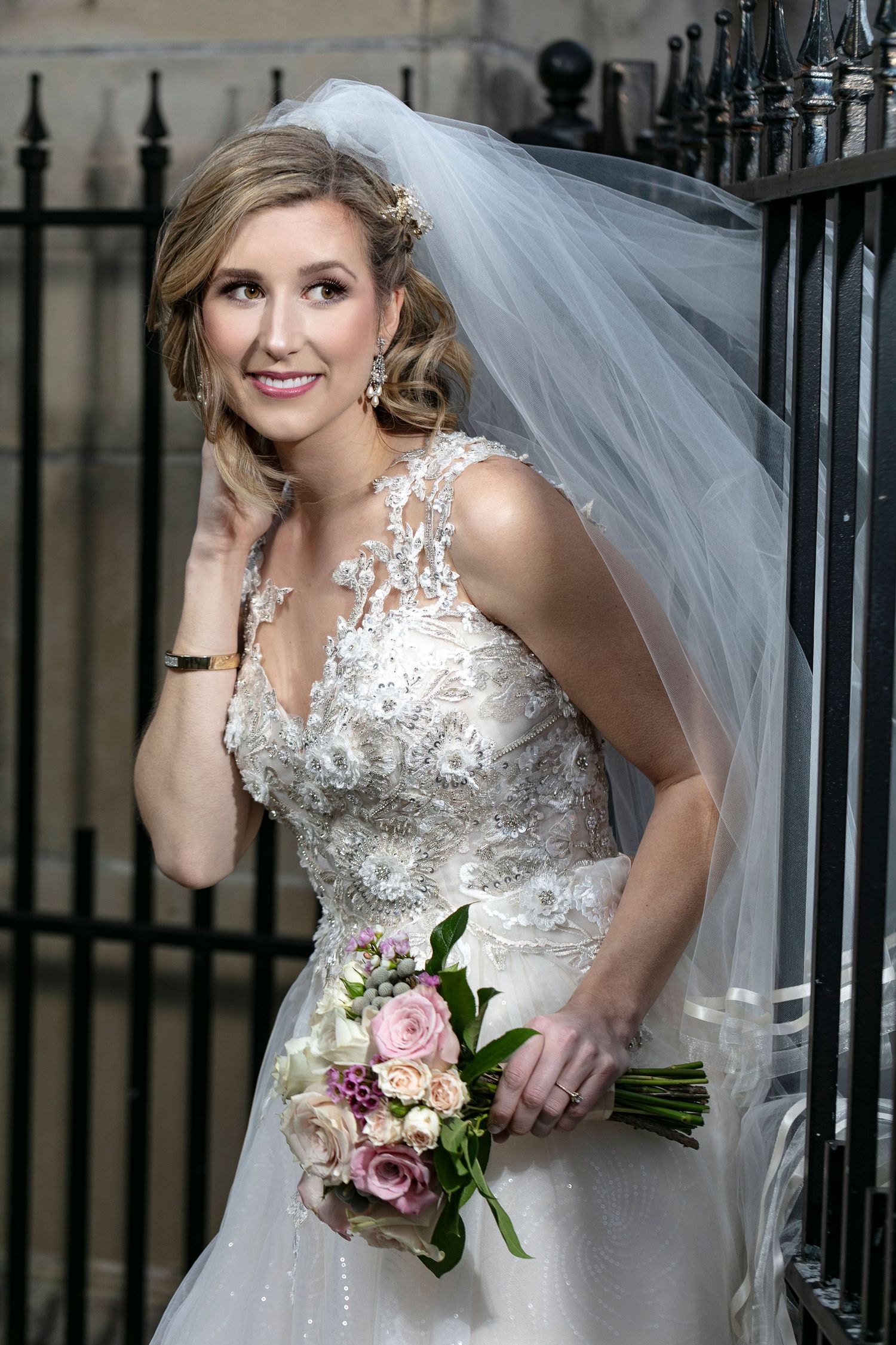Elegant bridal portraits showcase a detailed lace wedding dress and pink rose bouquet against iron gates.