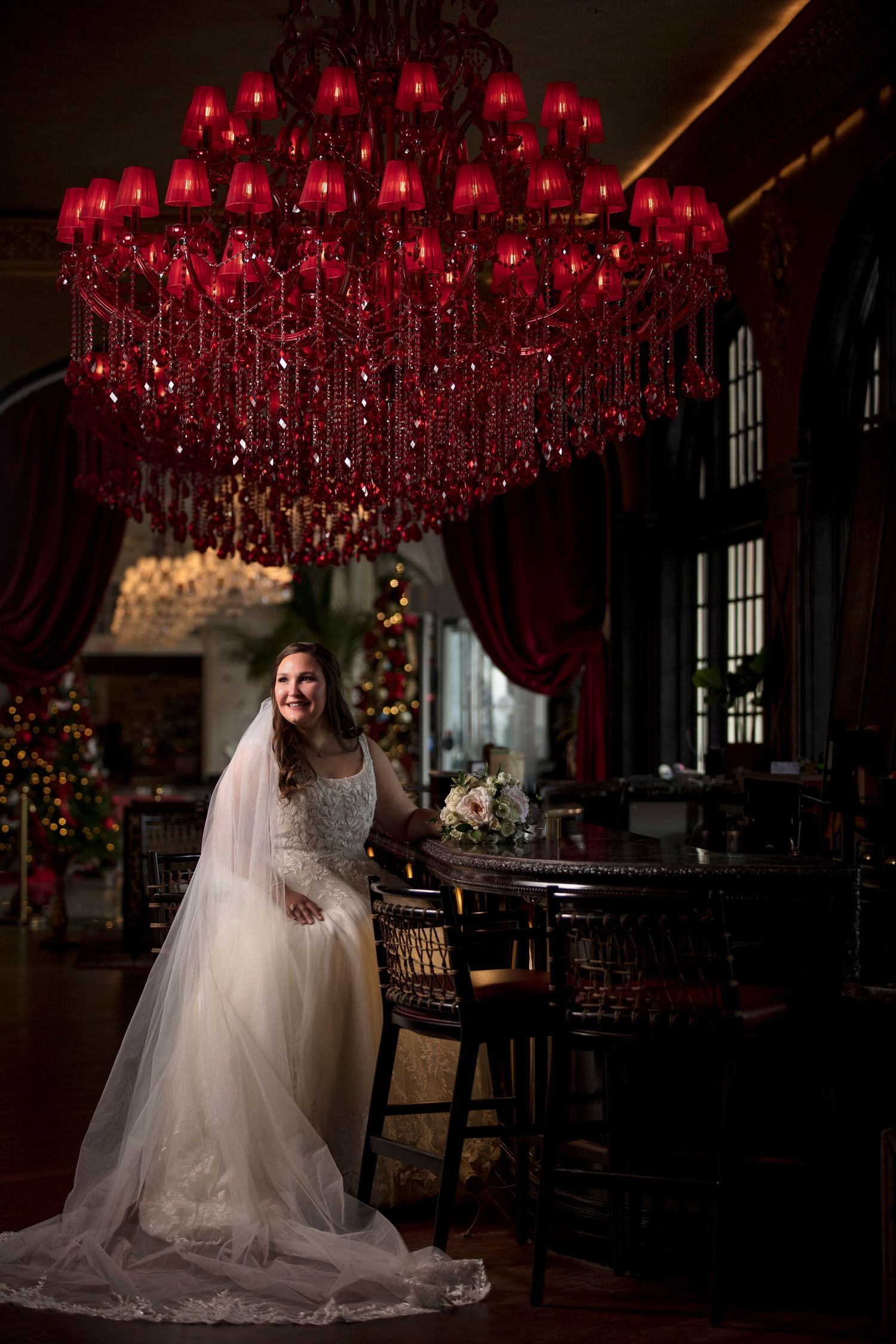 Dramatic bridal portrait under red chandelier lights in a dark, elegant venue.