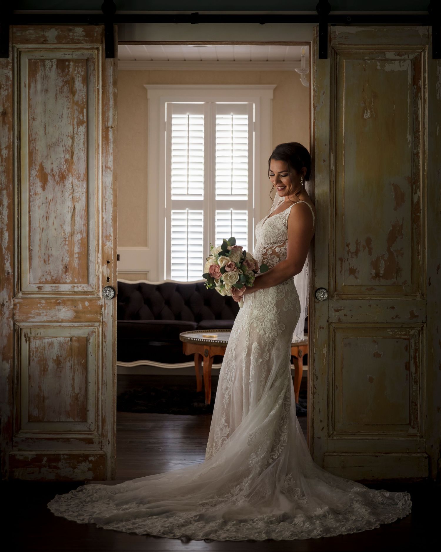 Bride in lace wedding gown posing in vintage room with distressed walls and shutters.