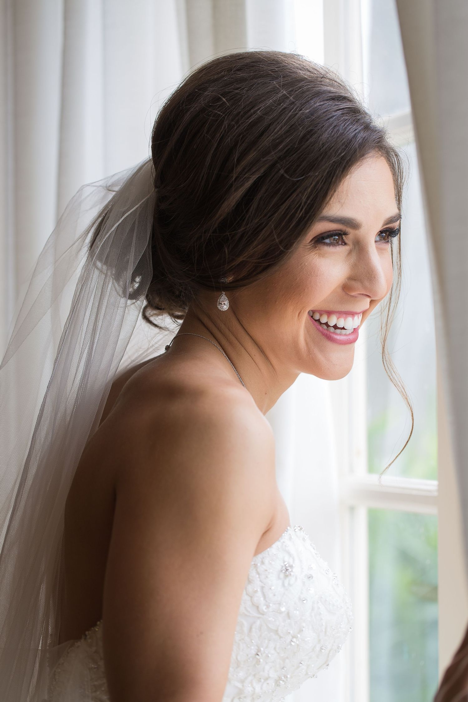 Ethereal bridal portrait by a window with soft white curtains creating a dreamy atmosphere.