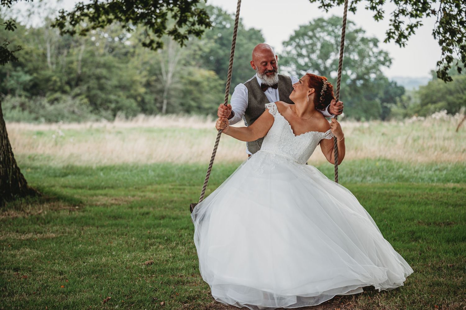 A joyful moment captured on a tree swing during a countryside wedding celebration.