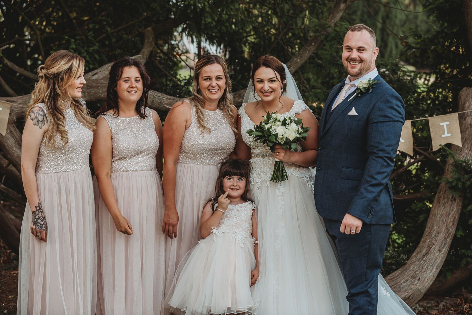 Wedding party in light colored formal attire pose for a portrait outdoors.