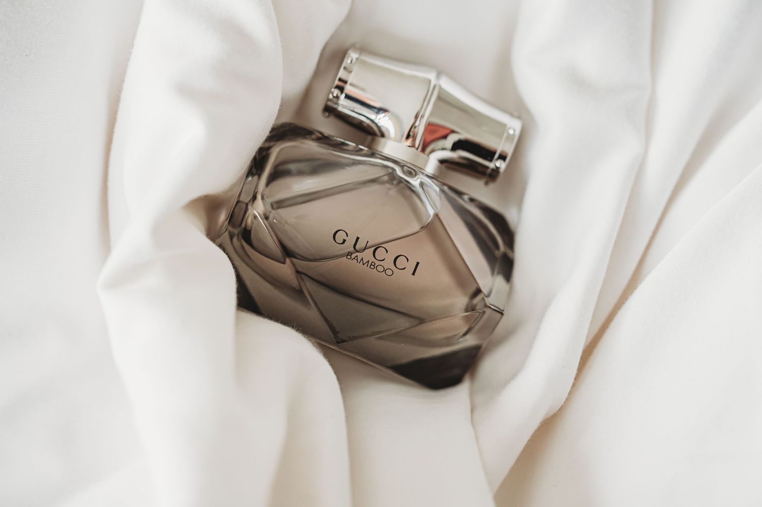 Gucci perfume bottle elegantly displayed on white silk fabric.