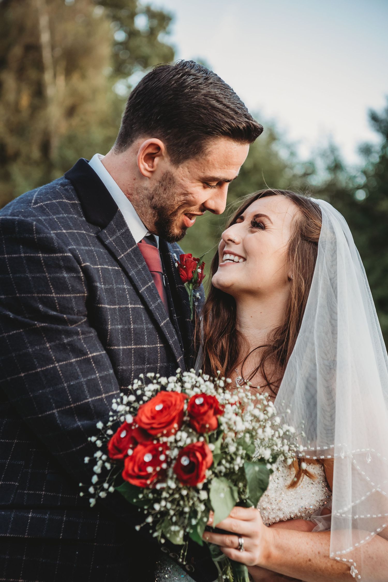 Intimate wedding portrait with couple sharing romantic moment amid red rose bouquet.